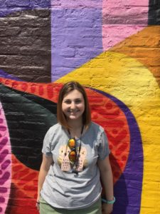 Rachel smiling at camera, standing in front of colorful outdoor wall 