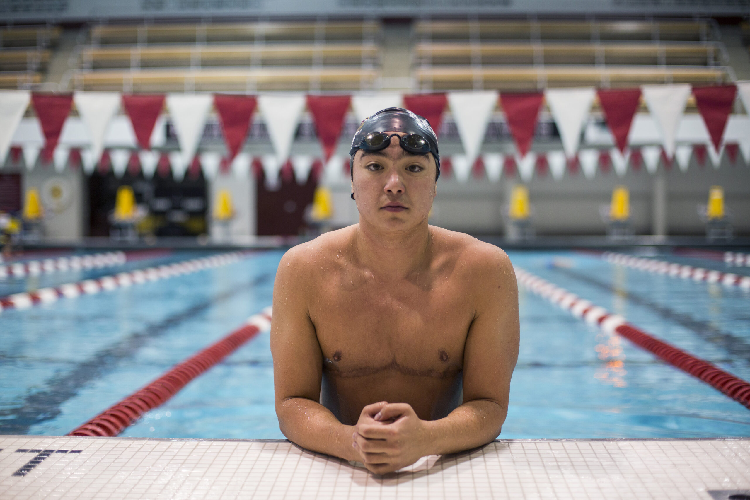 Foto de Schuyler (joven adulto mestizo) apoyando los brazos en el borde de la piscina, con el gorro de natación puesto y las gafas sobre la frente.